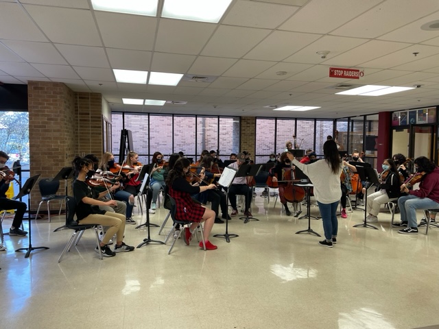 Taft orchestra students playing instruments in school foyer being director by orchestra director