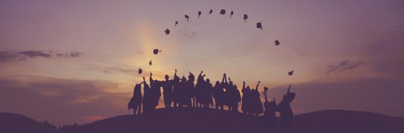 Image of students throwing graduation caps in air at dusk