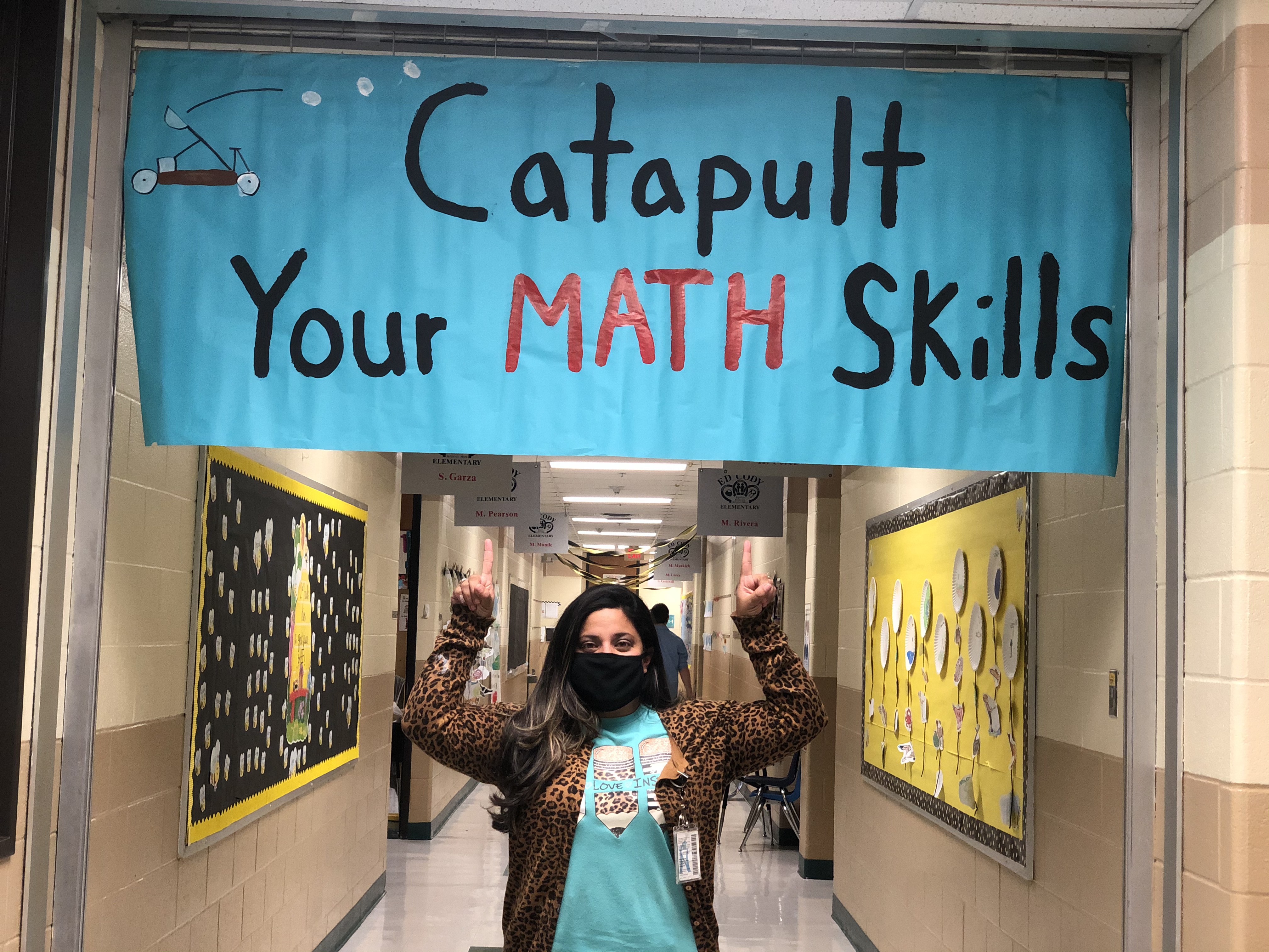 Female teacher pointing up to sign saying Catapult Your Math Skills.