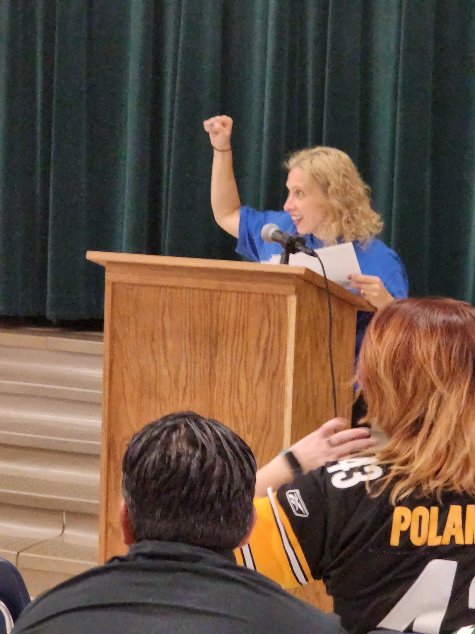 Blonde headed female standing at a podium speaking.
