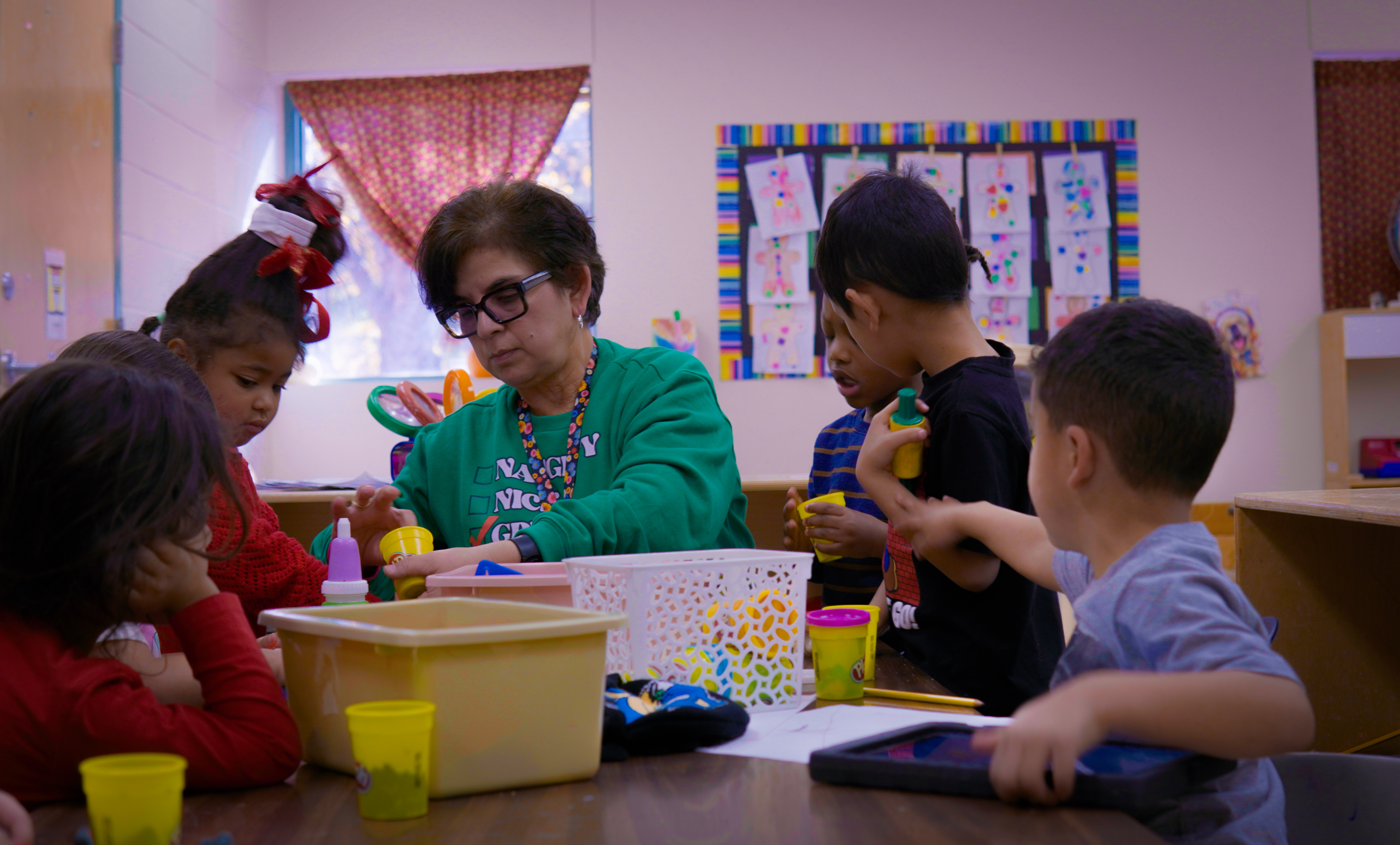 Pre-K Teacher, Ms Zamorano, sitting at a table with her students