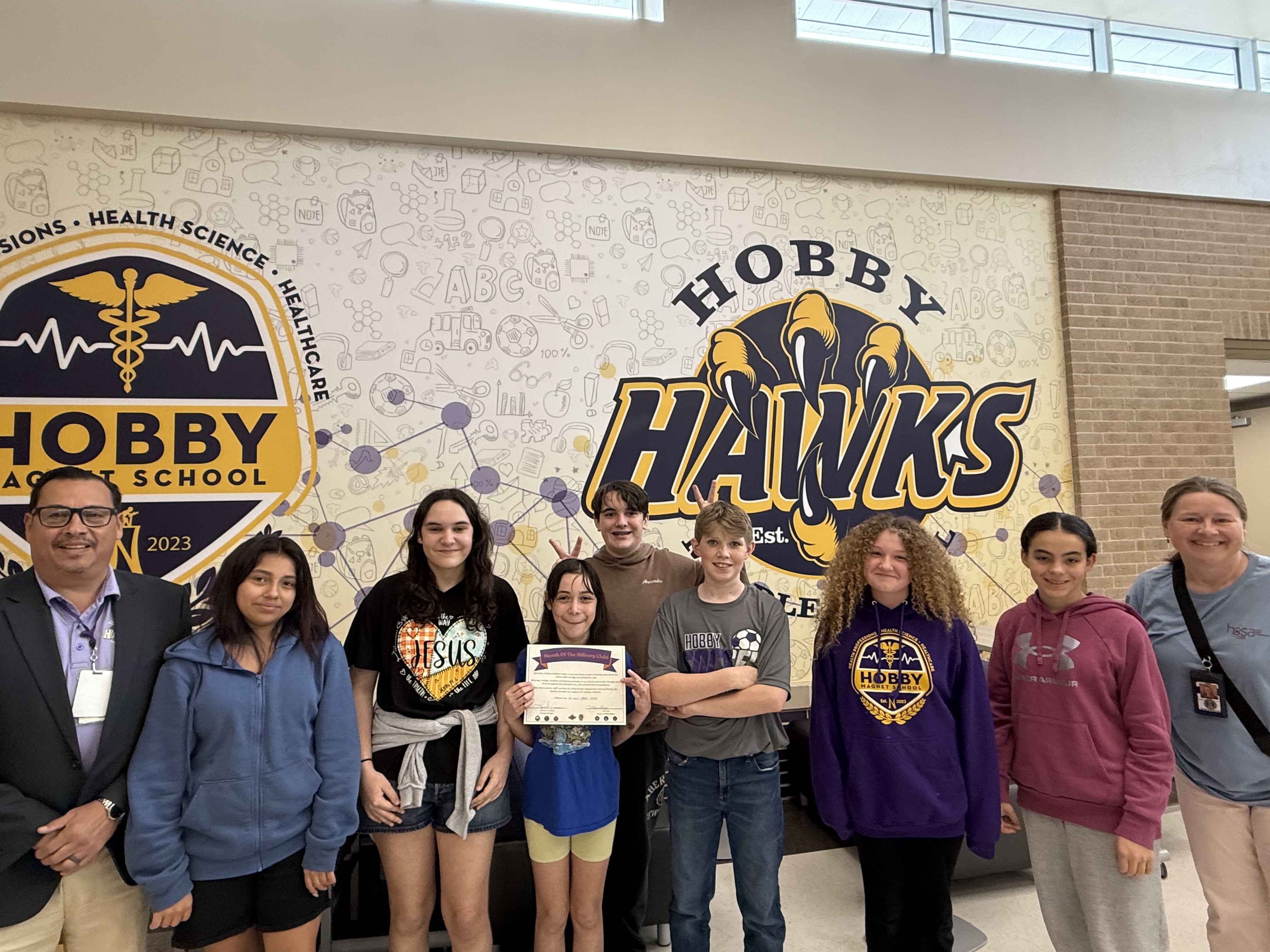 Picture of military connected children with 2 administrators standing in front of Hobby MS logos on wall