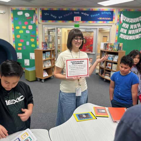 Ms. Mosley holding a sign about communication accessibility and talking to students.