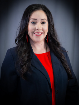 A white woman with black hair wearing a red blouse and blue jacket.