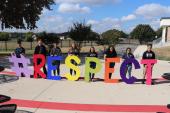 Students hold giant wooden letter outside that spell out RESPECT