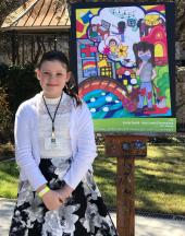 Emily poses outside with a picture of her winning artwork on an easel 
